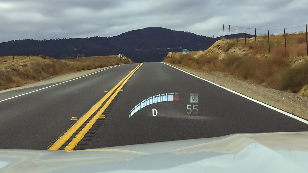 Driver’s view of a two-lane highway with a head-up display on the windshield showing a 55-mph speed limit sign and the gear indicator.