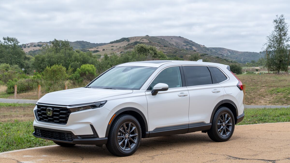 2026 Honda CR-V left-side front 3/4 view in white with green hills in the background under cloudy skies.