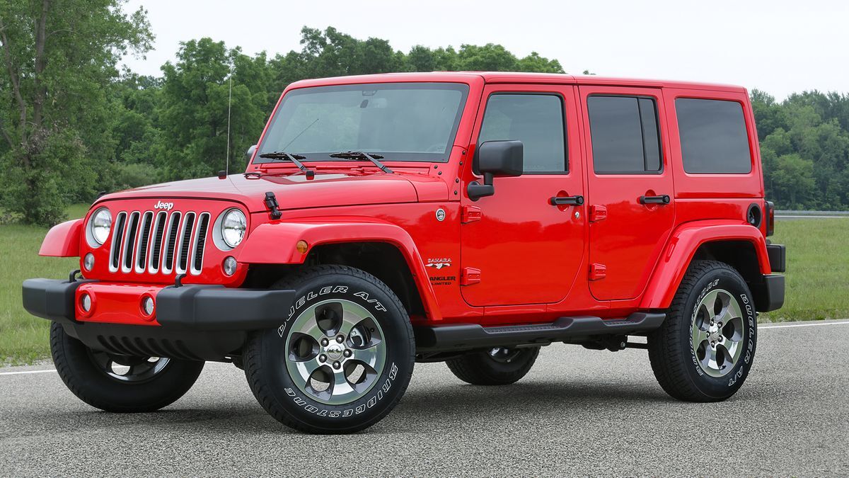 2017 Jeep Wrangler Sahara parked on asphalt with greenery in the background.