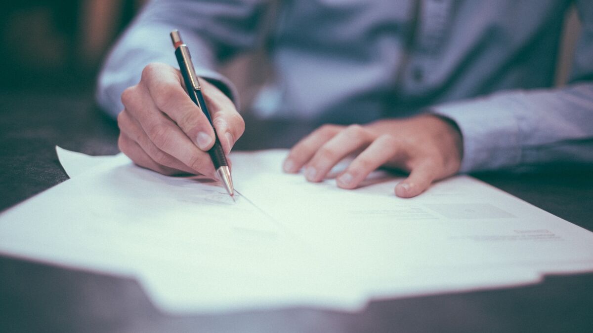 A stock photo showing a man in a blue dress shirt signing documents