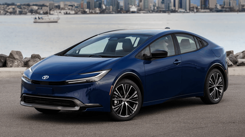 A blue 2026 Toyota Prius limited in a left-side 3/4 view with a bay in the background and asphalt in the foreground.