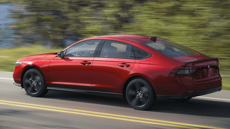 Red Honda Accord Hybrid Sport viewed from the rear 3/4 driver-side view against a blurred green background on a highway.